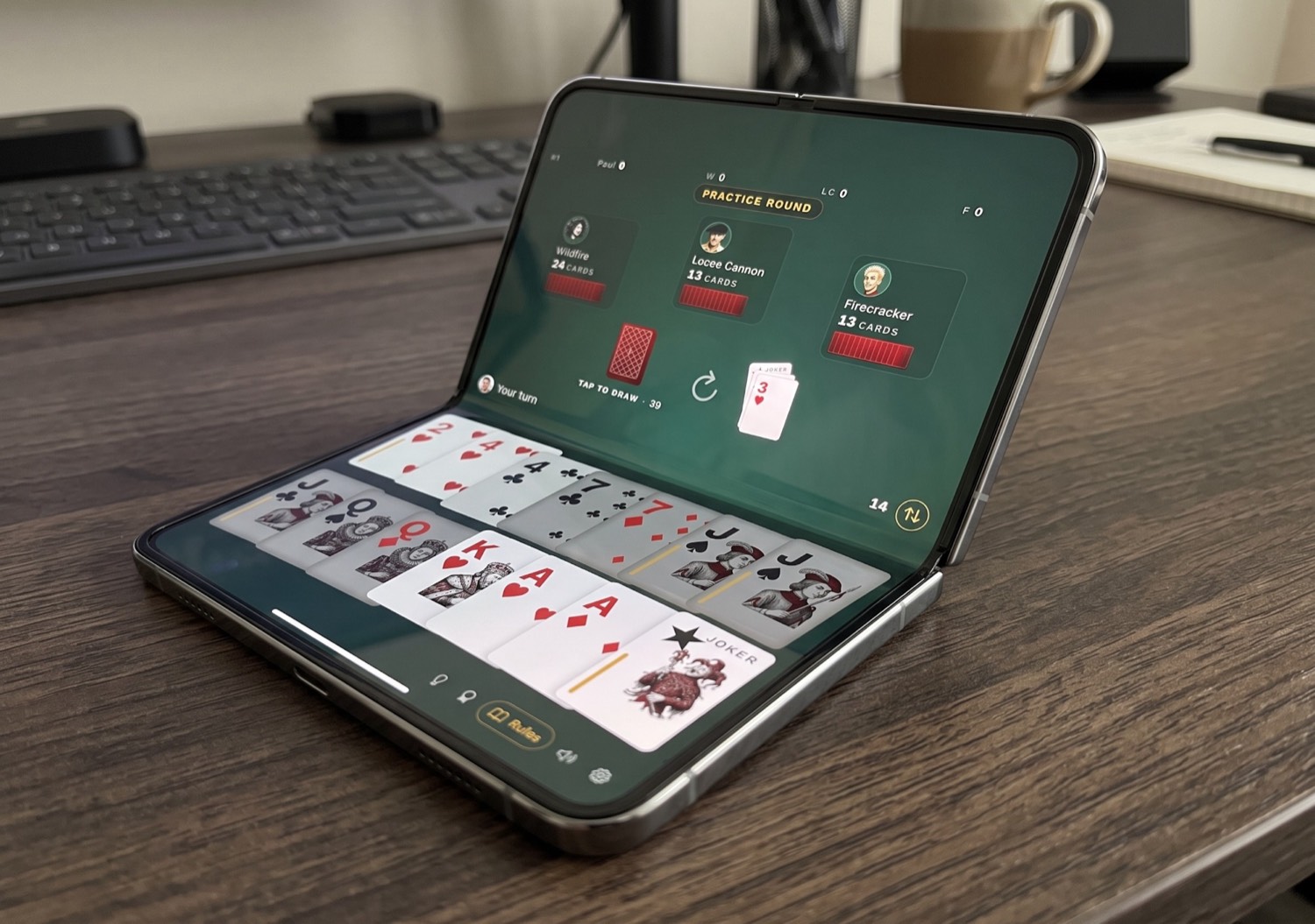 Foista on an iPhone Duo propped like a laptop — the card table on the upper screen, the player's hand on the lower screen